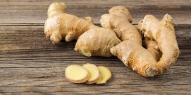 Raízes de gengibre frescas sobre superfície de madeira, com algumas fatias cortadas à frente.