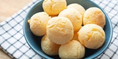 Comida Mineira Imagem de um bowl azul com pães de queijo sobre um pano xadrez.
