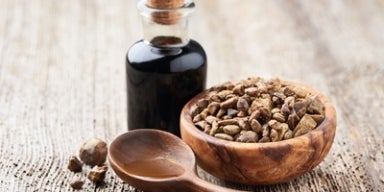 Benefícios do própolis para a saúde Frasco de vidro com própolis, tigela de madeira com pedaços de própolis e colher de madeira sobre superfície rústica.