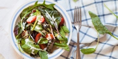 Bowl de salada verde com tomates e molho de iogurte sobre um pano xadrez branco e azul.