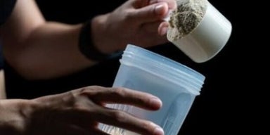 Mulher segurando um copo de plástico com Whey Protein, e com a outra mão segura um medidor cheio da mesma proteína.