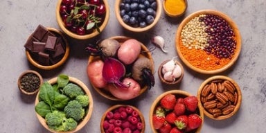 Tigelas com frutas, vegetais, sementes e chocolate amargo, representando alimentos ricos em antioxidantes naturais.