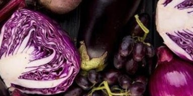 Alimentos roxos, incluindo legumes e frutas como cebola, berinjela, repolho e beterraba misturados em cima de uma mesa.