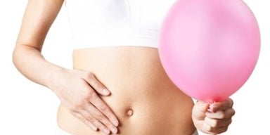 Barriga inchada: o que fazer para desinchar? Mulher com a mão na barriga segurando um balão rosa representando barriga inchada.