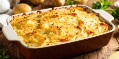 Travessa de batata gratinada dourada, servida em recipiente de cerâmica, decorada com salsa, sobre mesa rústica de madeira.