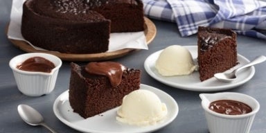Bolo de chocolate servido com bolas de sorvete de creme e cobertura, acompanhado de pequenas tigelas com calda de chocolate.
