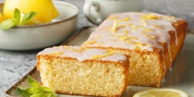 Bolo de limão com cobertura glaceada e raspas de limão, servido em fatias sobre bandeja com limão fresco ao lado.