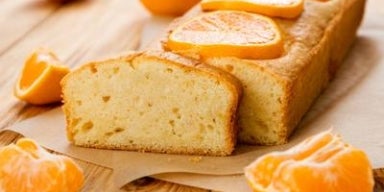 Receitas com tangerina Bolo retangular de tangerina com gomos de tangerina e uma fatia cortada.