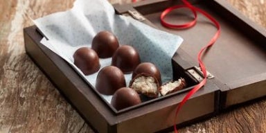 Bombons de chocolate com recheio de coco em caixa de madeira decorada com fita vermelha.