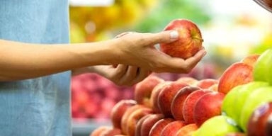 Mão segurando uma maçã como se estivesse escolhendo frutas.