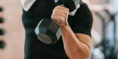 pessoa com blusa preta e uma toalha de rosto em volta do pescoço, segurando um halter com os cotovelos flexionados.