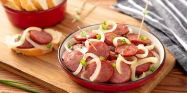 Prato de linguiça acebolada servido em tigela vermelha, acompanhado de fatias de pão ao fundo.