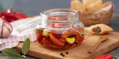 Pimenta em conserva caseira com alho e azeite em pote de vidro sobre tábua de madeira.