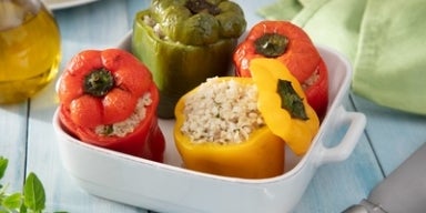 Pimentões vermelhos, amarelo e verde recheados com arroz em uma travessa branca sobre mesa azul.