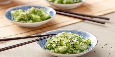 Salada sunomono de pepino japonês com gergelim servida em prato azul e branco.