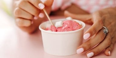 Tomar sorvete gripado faz mal? Mãos de uma mulher segurando um pote branco de sorvete com a cor rosa. A imagem representa a dúvida se tomar sorvete gripado