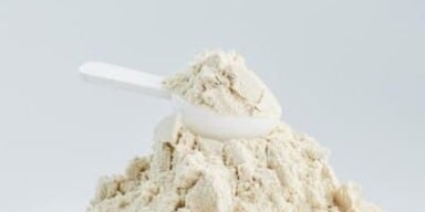 Whey protein substitui refeição? Whey protein em pó em cima de uma mesa branca, junto a um scoop. A imagem representa se whey substitui refeição.