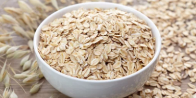 Benefícios da aveia: intestino e flora intestinal Bowl branco com aveia e grãos de aveia em volta.