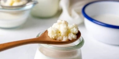 Benefícios do kefir: 6 propriedades desse alimento Colher de madeira com kefir sobre um copo de leite.
