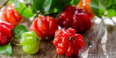 Benefícios da pitanga: você sabe como a pitanga pode te ajudar? Pitangas maduras e verdes com folhas sobre uma superfície de madeira.