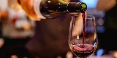 Brinde à saúde: 5 benefícios e 5 malefícios do vinho Vinho tinto sendo servido em taça de vidro, com fundo desfocado, representando os benefícios do vinho.
