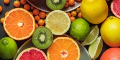 Frutas cítricas variadas como laranja, limão, kiwi e grapefruit cortadas ao meio, dispostas em fundo escuro.