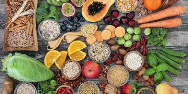 Alimentos ricos em fibras como frutas, legumes, grãos integrais, sementes e castanhas organizados sobre mesa rústica.
