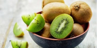 Kiwis inteiros e cortados ao meio em tigela, com polpa verde vibrante e sementes aparentes.