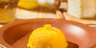  Cuscuz amarelo servido em prato de barro, ainda quente, sobre mesa rústica.