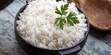Arroz branco cozido em panela preta, finalizado com folha de salsa, sobre superfície rústica.