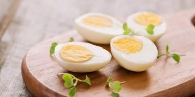 Ovos cozidos cortados ao meio sobre tábua de madeira, com gema firme e folhas verdes.