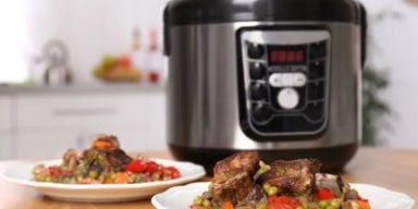 Prato com carne e legumes servido à frente de uma panela de pressão elétrica sobre a bancada.