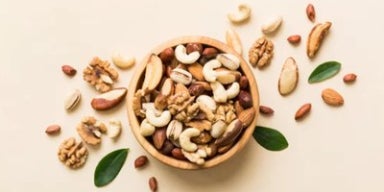 Mix de castanhas e nozes em tigela de madeira, com amêndoas, castanha-de-caju e nozes sobre fundo claro.