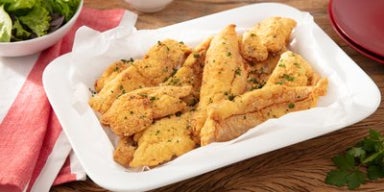 Tiras de frango empanado com ervas, servidas em travessa branca sobre mesa de madeira.