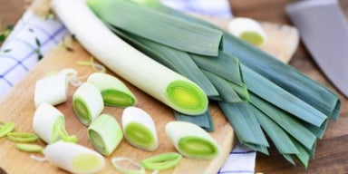 Alho-poró inteiro e fatiado sobre uma tábua de madeira, mostrando o ingrediente fresco para preparo de receitas.