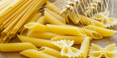 Massas secas italianas dos tipos espaguete, penne e farfalle com espigas de trigo em composição culinária.