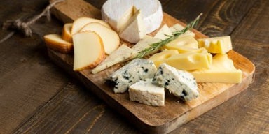 Tábua de madeira com variedade de queijos, incluindo brie, queijo azul, suíço e defumado.