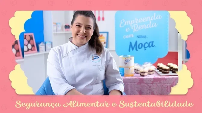 Fotografia com tons rosa, azul e amarelo, com uma mulher de cabelo preso, sorridente. Ao fundo docinhos expostos em uma mesa.