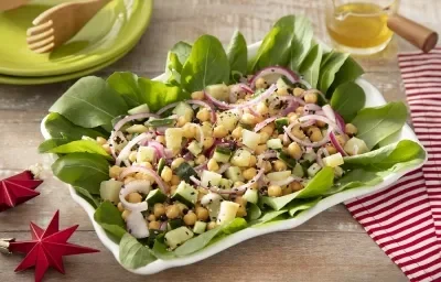 Foto em tons vivos da receita de salada de grão de bico e batata doce servida em um prato grande retangular de porcelana branca sobre uma mesa de madeira com um paninho listrado vermelho ao lado Foto em tons vivos da receita de salada de grão de bico e batata doce servida em um prato grande retangular de porcelana branca sobre uma mesa de madeira com um paninho listrado vermelho ao lado