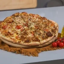Foto da receita de massa básica de pizza, servida numa tábua de madeira com o sabor de pizza salgada. A tábua está ao lado de um galeteiro de azeite e alguns tomates.