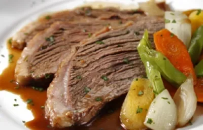 Fotografia em tons de marrom em uma mesa com um pano laranja e um prato raso branco em cima com duas fatias de picanha e os legumes.