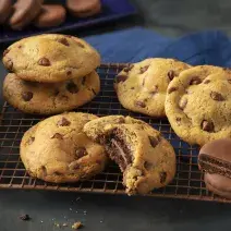 Fotografia em tons de preto e azul de uma bancada preta com um grade dourada, sobre ela cookies. Ao fundo um paninho azul e biscoitos negresco cobertos de chocolate espalhados.
