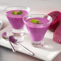 Foto da receita de Mousse de Pitaya e Leite Moça. Observa-se duas taças de vidro com a mousse cor-de-rosa decorada com hortelã em cima de um prato branco quadrado.