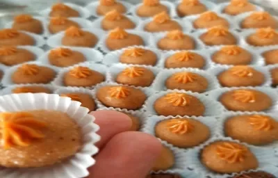 Foto em tons de laranja da receita de brigadeiro de churros servida em várias porções, com destaque para uma unidade sobre os dedos de uma pessoa a frente Foto em tons de laranja da receita de brigadeiro de churros servida em várias porções, com destaque para uma unidade sobre os dedos de uma pessoa a frente