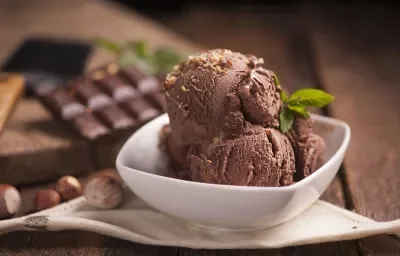 fotografia em tons de branco e marrom tirada de frente. Contém um recipiente quadrado branco com bolas de sorvete de chocolate.