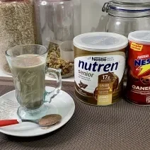 Imagem da receita de Cappuccino Proteico, sobre uma mesa, ao lado uma lata de Nutren Protein e Nescau Canela