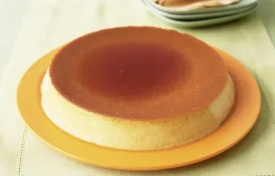 Fotografia de um pudim com calda de caramelo por cima, servido em um prato amarelo sobre uma mesa de madeira Fotografia de um pudim com calda de caramelo por cima, servido em um prato amarelo sobre uma mesa de madeira