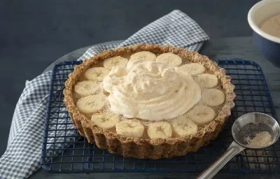 Foto da receita de banoffee de farinha lactea aveia servida em uma porção grande sobre uma grade preta com uma colher de servir prateada ao lado