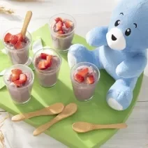 Foto da receita de Iogurte de Morango. Observa-se 5 tacinhas de vidro com o iogurte e morangos picados dentro, dispostos sobre uma tábua verde.