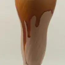 Fotografia em tons de marrom em uma bancada cinza com uma taça de vidro alta e o milkshake de chocolate dentro dela.